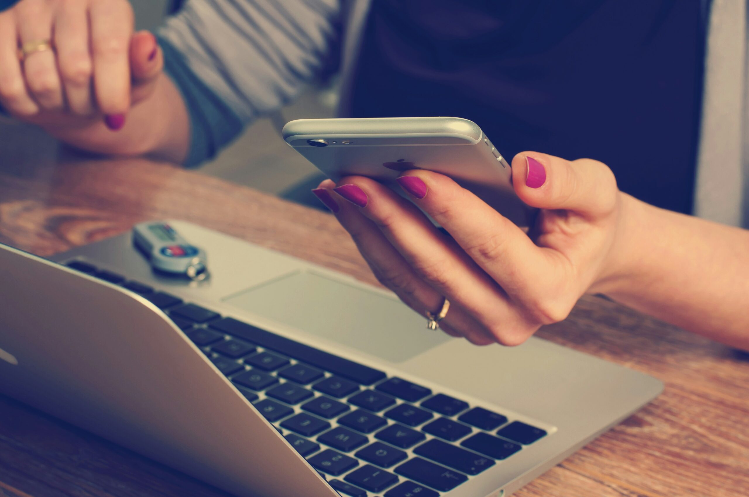 una mujer con un teléfono en la mano frente a un portátil mirando su página web